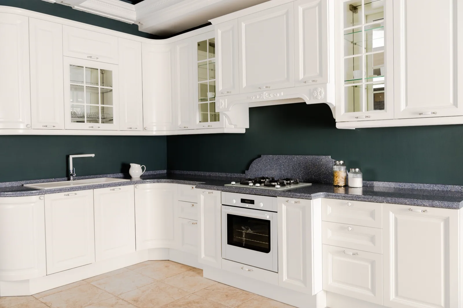White painted raised-panel kitchen cabinets with glass-front uppers against a deep green wall