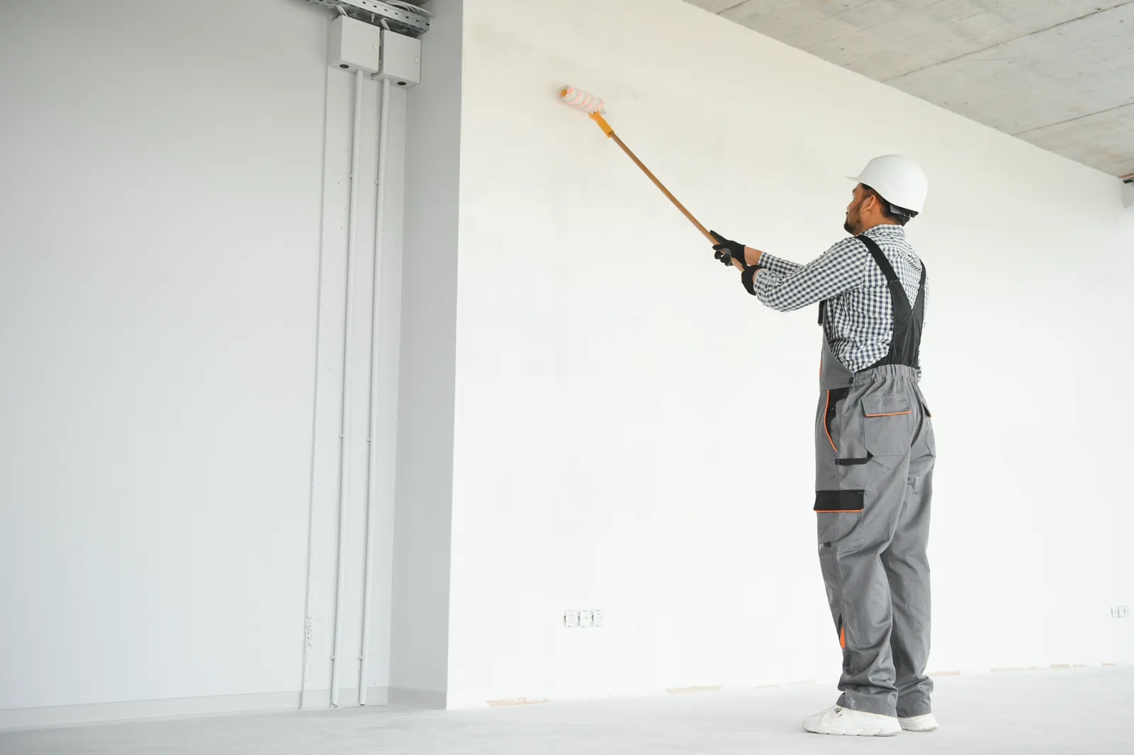 Painter rolling primer onto new white drywall in an open room