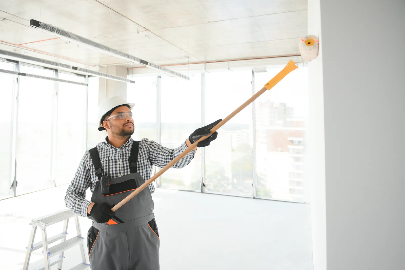 Painter rolling fresh paint onto new drywall in a bright room