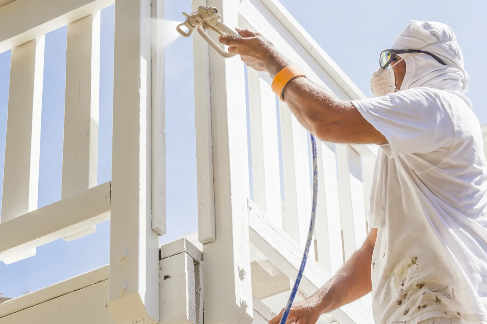 Painter spraying fresh white paint onto exterior wood railings