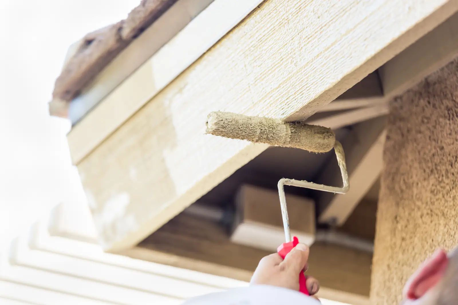 Roller applying paint to exterior wood trim