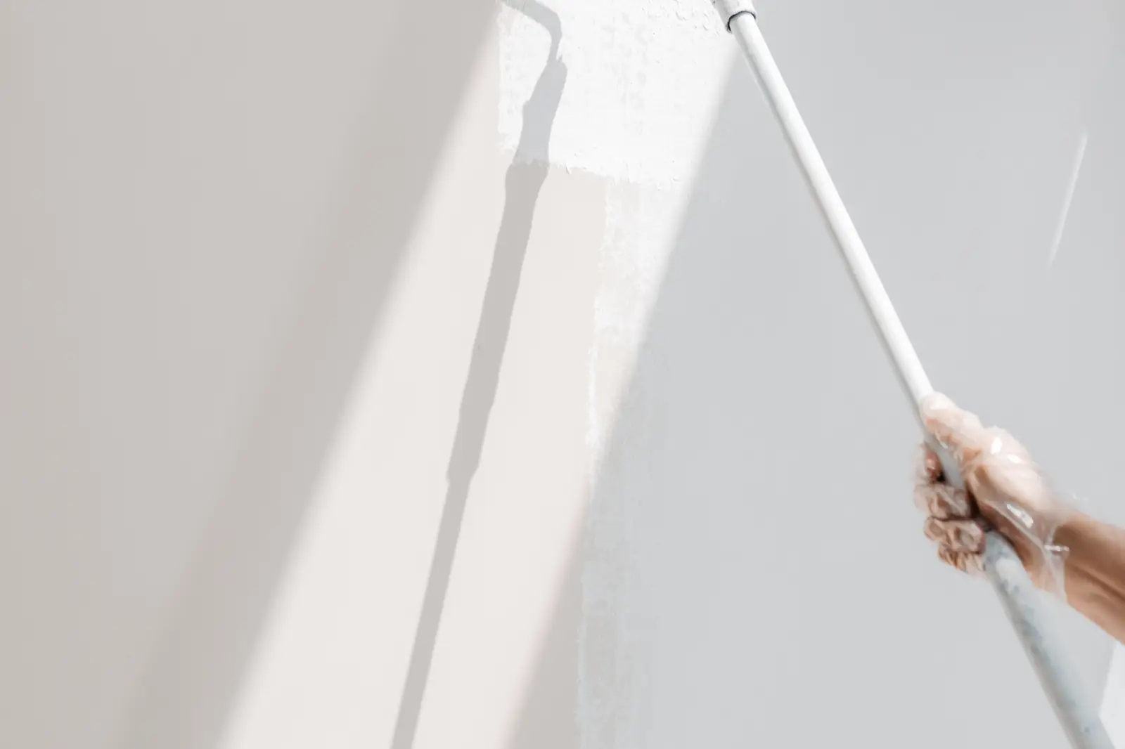 Painter rolling a fresh coat of white paint on drywall