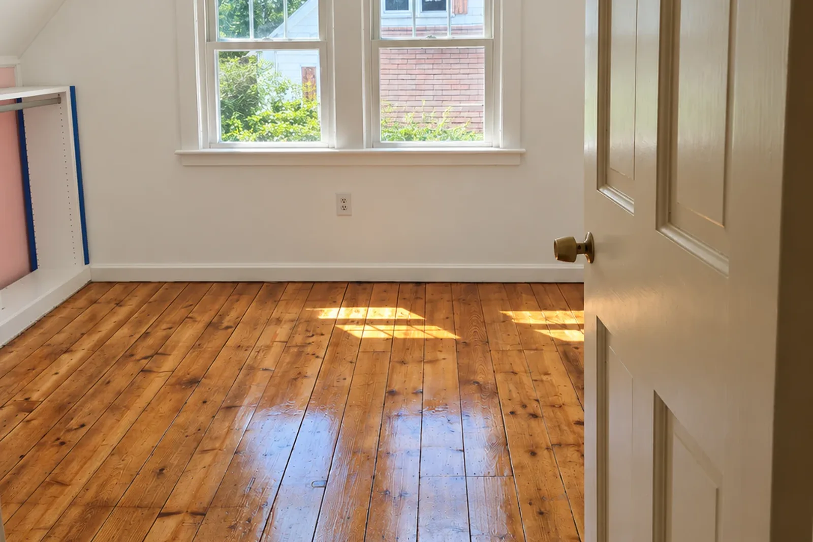 Refinished wide pine floorboards with a glossy amber finish in a bright attic bedroom